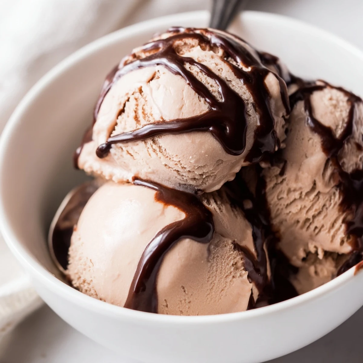 Velvety scoops of Chocolate Ice Cream with Warm Chocolate Sauce melt into a glass bowl, garnished with chocolate shavings.