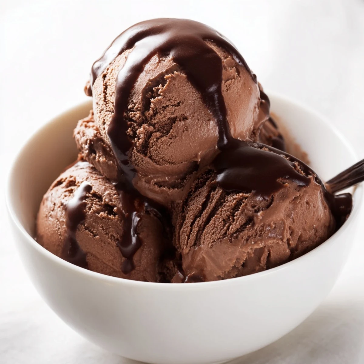 Creamy Chocolate Ice Cream with Warm Chocolate Sauce drizzled generously over a scoop in a rustic dessert bowl.