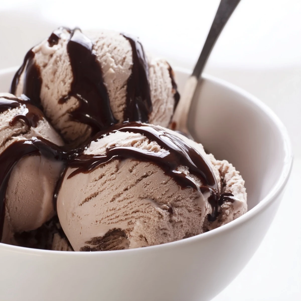 Decadent Chocolate Ice Cream with Warm Chocolate Sauce topped with chocolate curls, served beside a steaming mug.