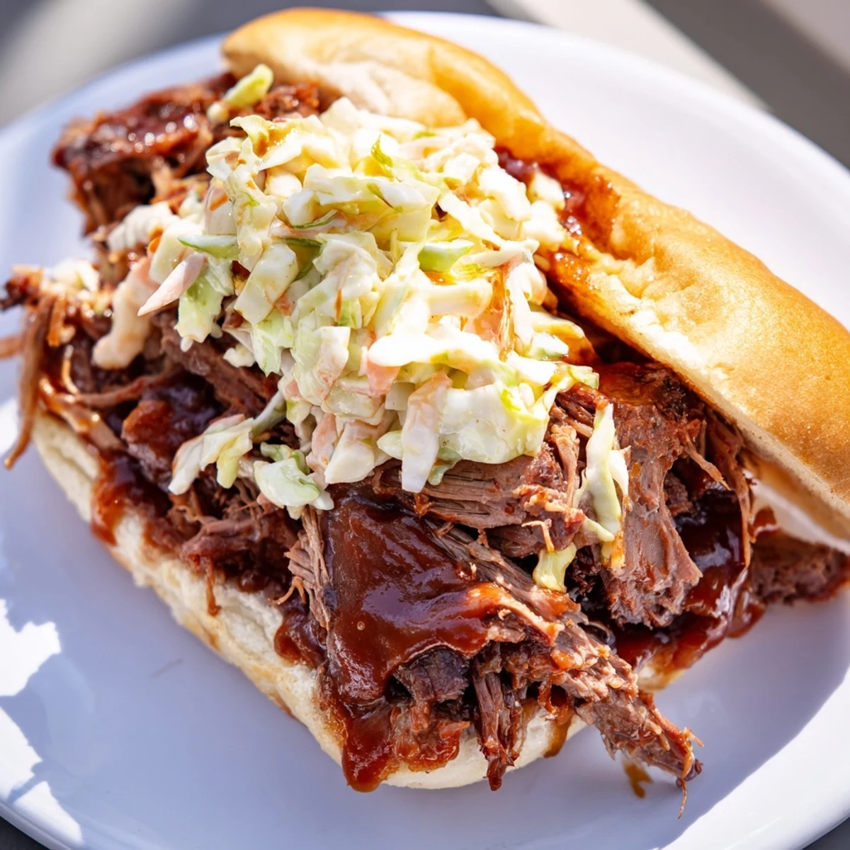 Steamy Slow Cooker Pulled Beef Sandwiches stacked on a plate with barbecue sauce and pickles.