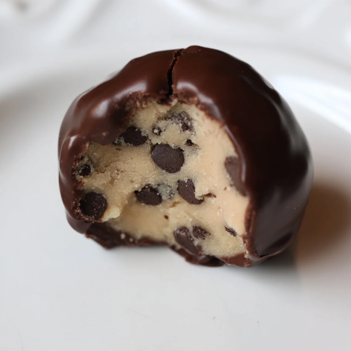 A hand dips a golden-hued Cookie Dough Truffle into a bowl of melted chocolate, ready for its decadent coating.