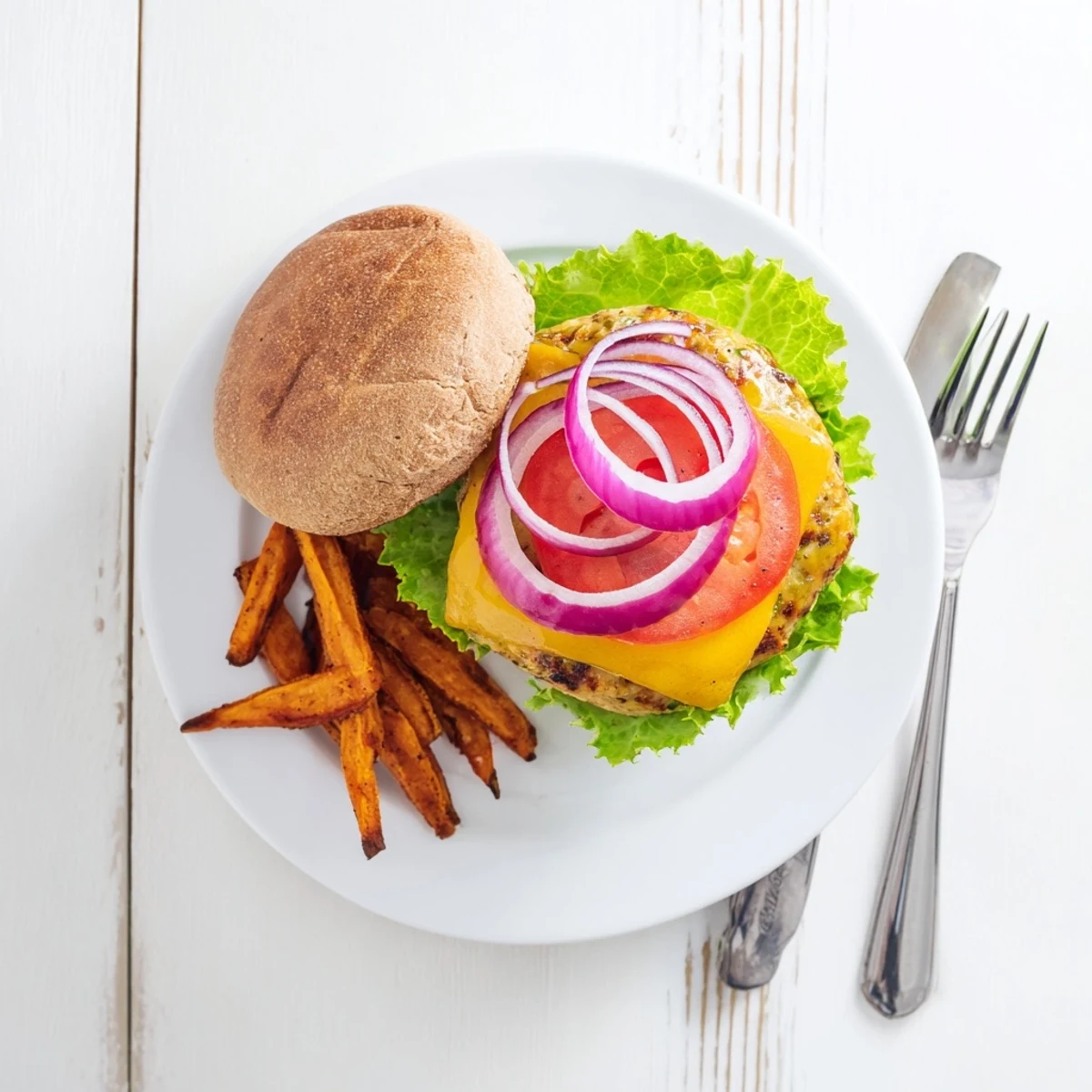 A juicy turkey burger topped with melted cheddar sits beside golden crispy sweet potato fries on a plate.  