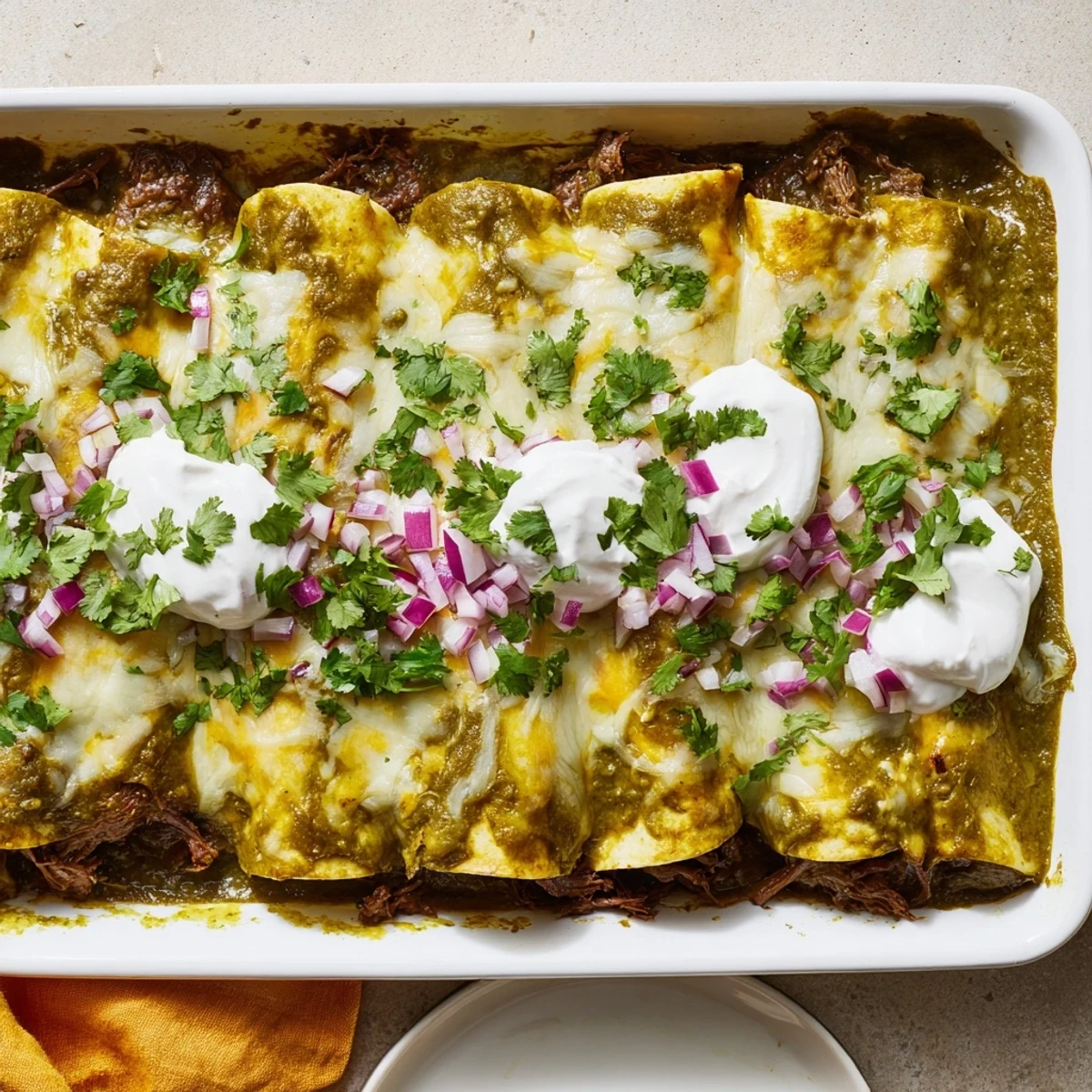 Golden baked enchiladas topped with creamy sour cream and fresh cilantro, showcasing the rich, tangy green sauce and tender beef filling inside.