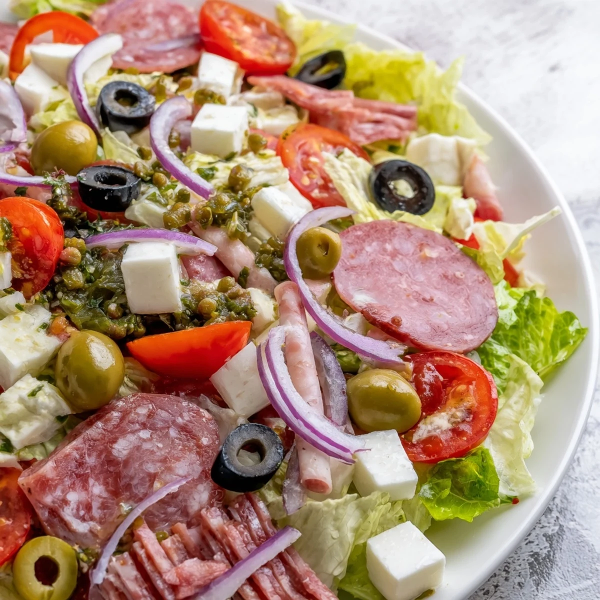 A vibrant serving of New Orleans Muffuletta Salad featuring crisp romaine, cured meats, cheeses, and a briny olive relish.