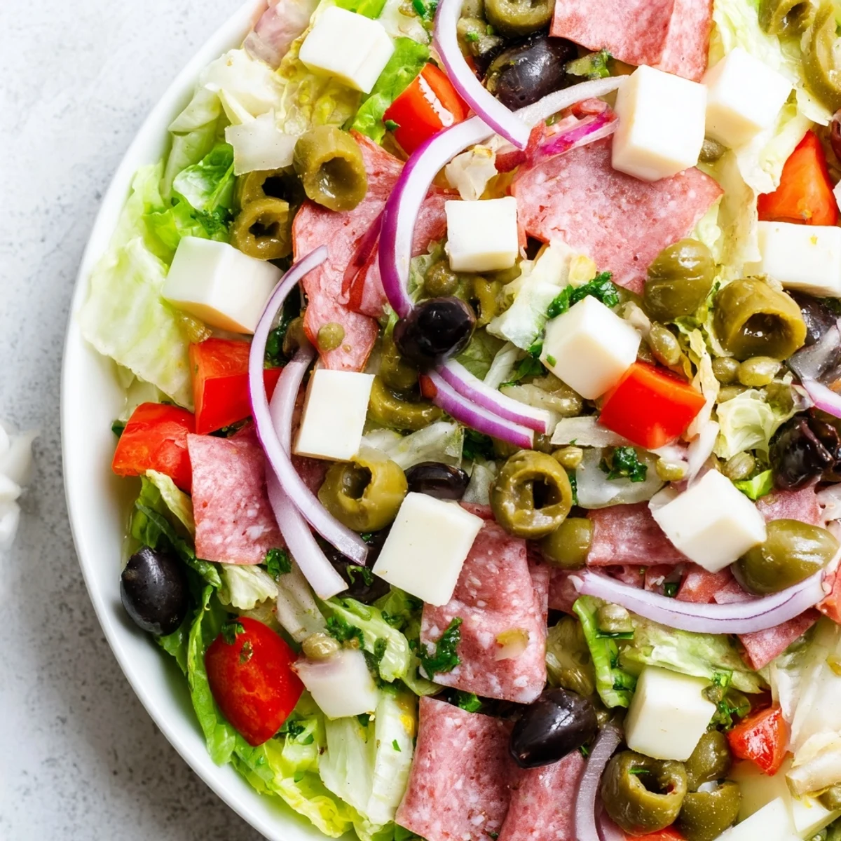A close-up of New Orleans Muffuletta Salad topped with chunky olive relish, juicy tomatoes, and fresh basil garnish.