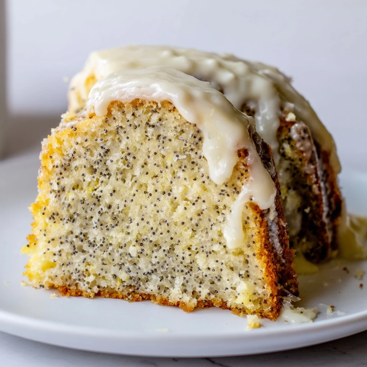 A freshly baked Lemon Poppy Seed Bundt Cake with Icing sits beside a cup of tea, highlighting its zesty glaze.