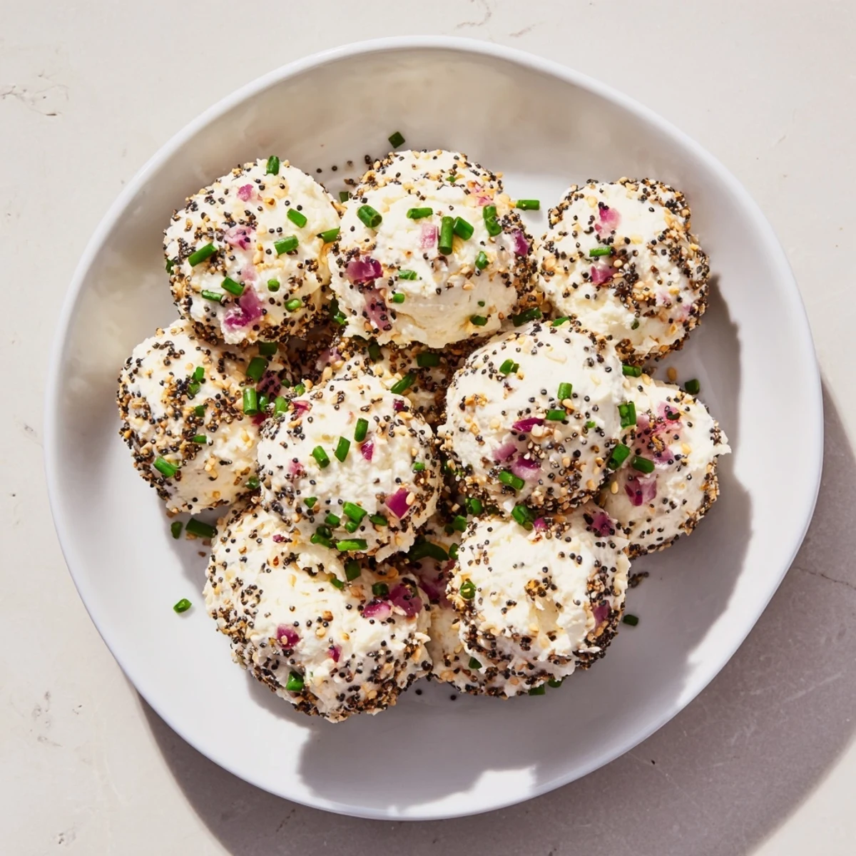 Soft creamy Everything Bagel Cottage Cheese Bites with chopped chives served alongside crisp cucumber slices.