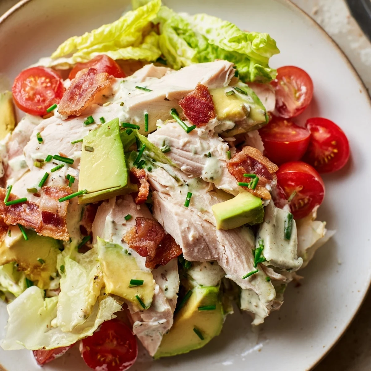 Serve this hearty BLT Chicken Salad topped with crumbled bacon and herbs on a white plate for a bright summer meal.