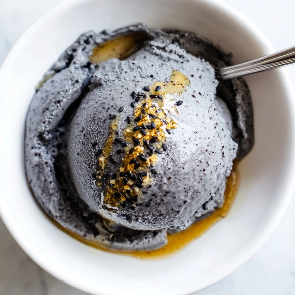 This homemade toasted black sesame ice cream features a rich, creamy scoop nestled in a rustic ceramic bowl, garnished beautifully for a photogenic food blog image.