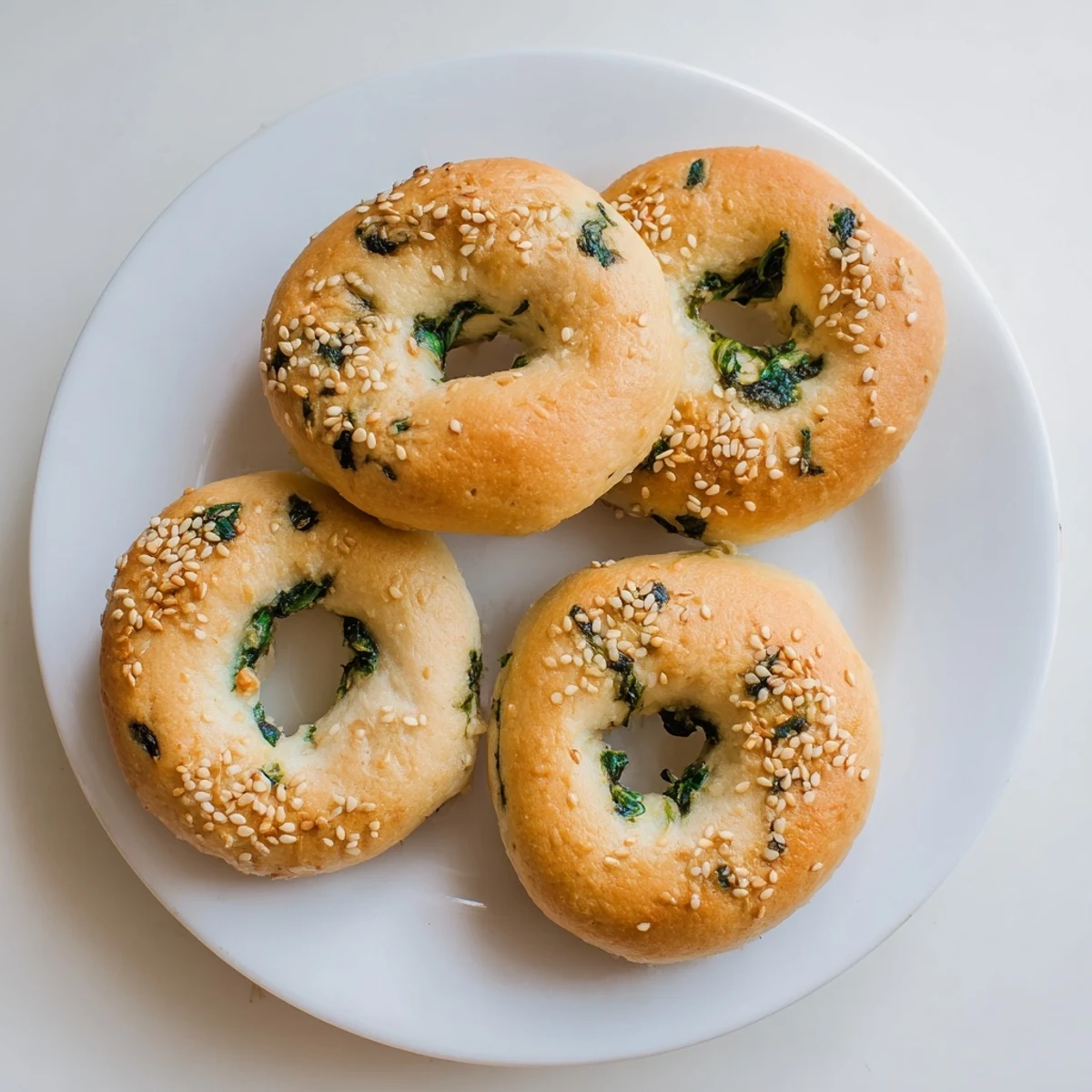 Golden-brown Spinach Cottage Cheese Flagels rest on a wire cooling rack, showcasing their flattened, chewy texture speckled with vibrant green spinach pieces.