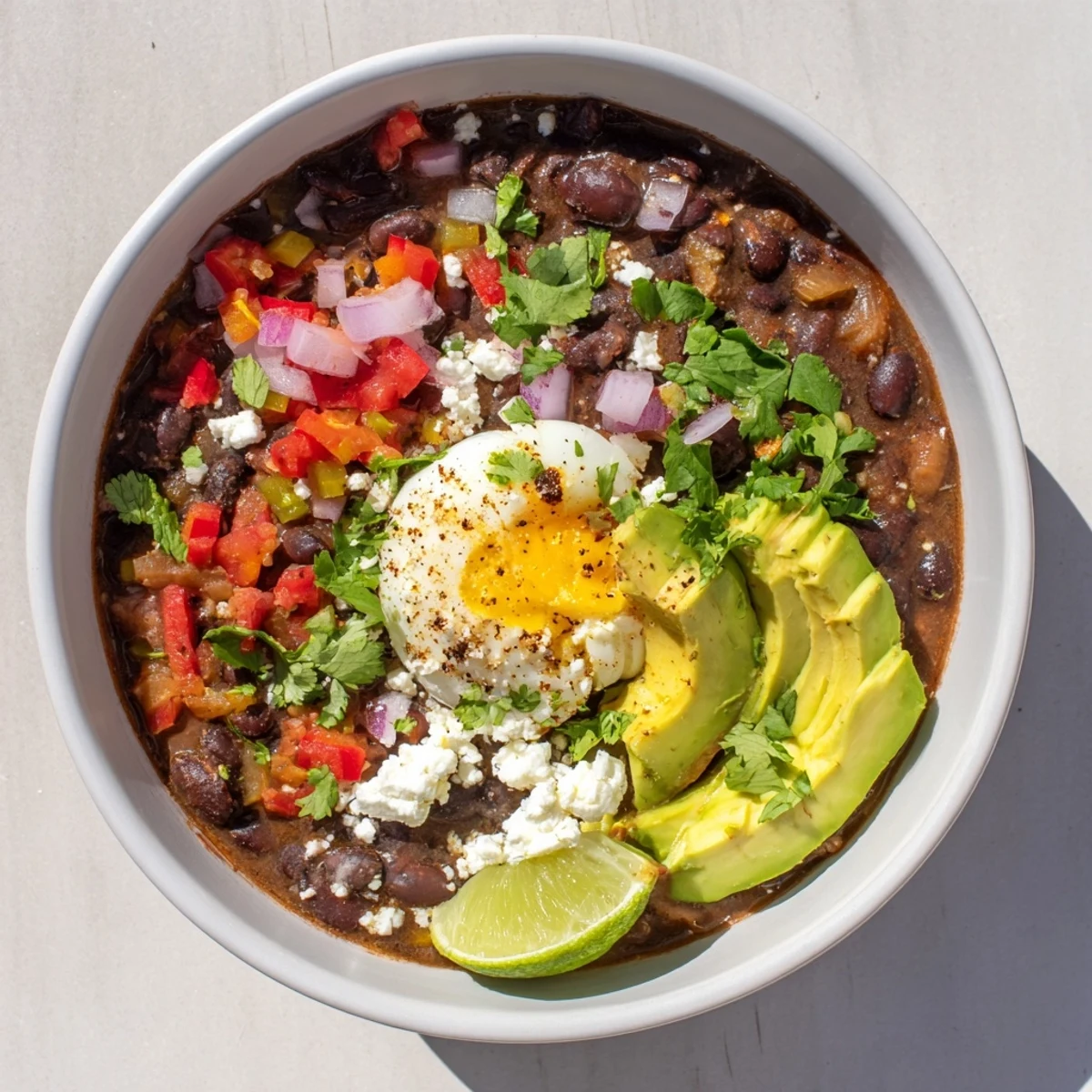 Creamy soft-boiled egg crowns steaming Mexican Braised Beans in a rustic bowl, garnished with avocado and cilantro.