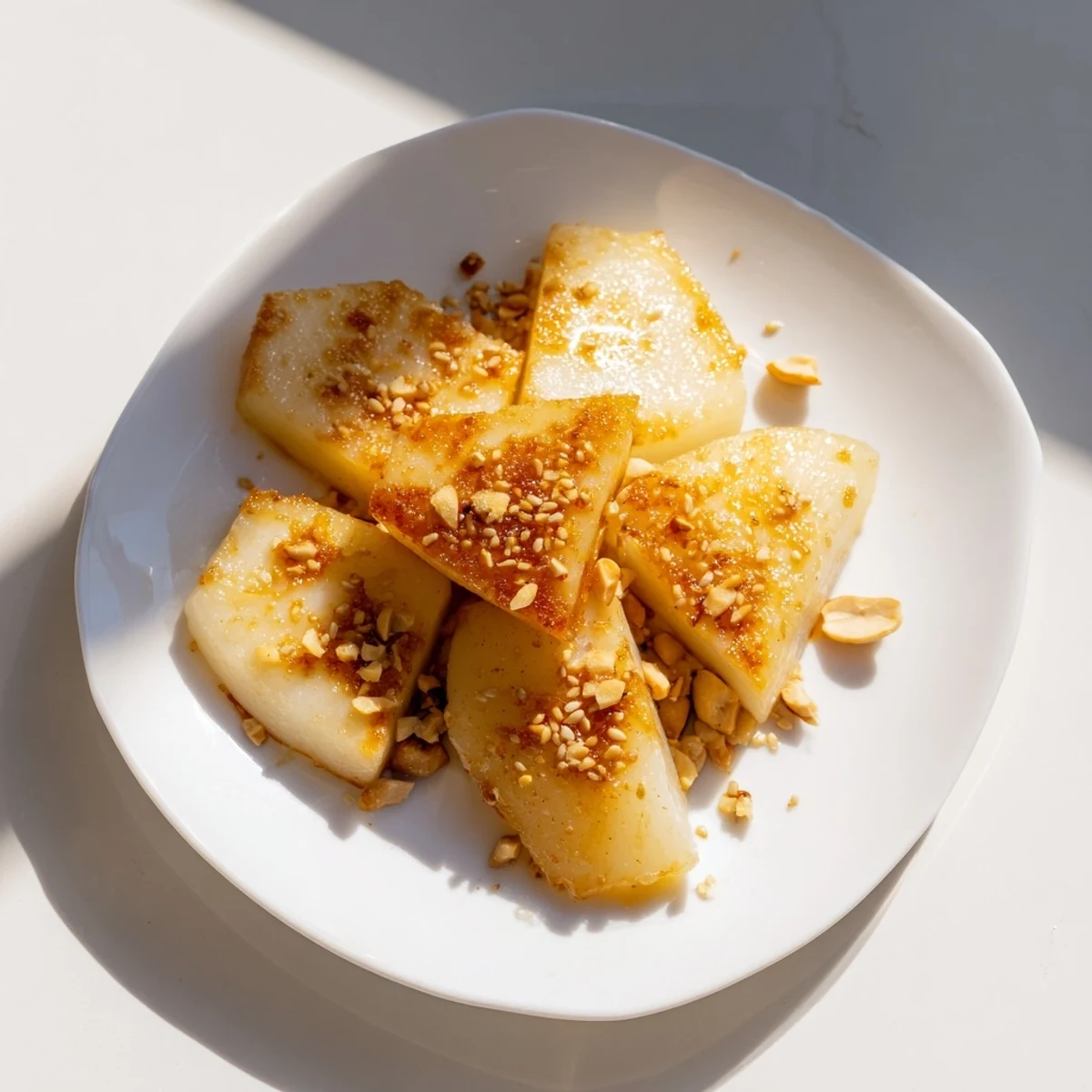 Golden Korean pan fried rice cakes coated in glossy sweet butter glaze with sesame seeds