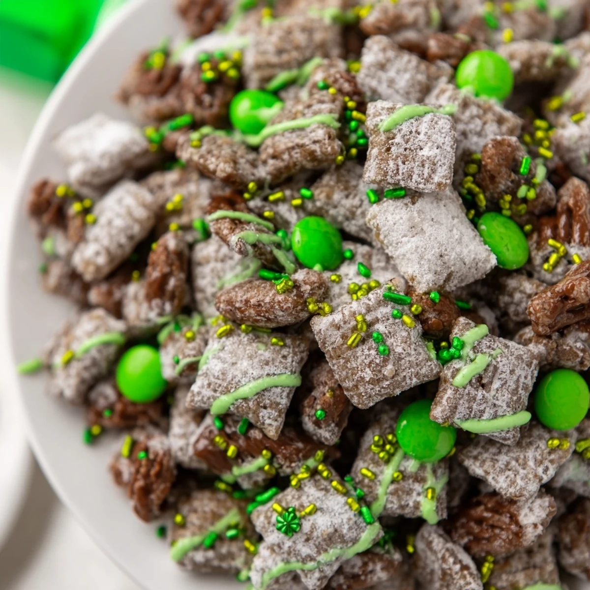 Green drizzled St. Patricks Day puppy chow mix with colorful candy-coated chocolates arranged on a rustic wooden board