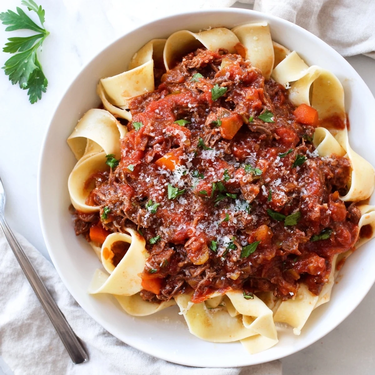 Slow cooker beef ragu with tender shredded meat in rich tomato sauce served over wide pasta