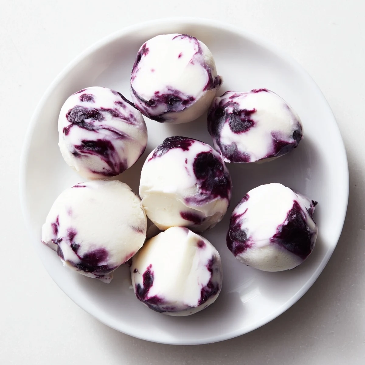 Frozen blueberry swirl yogurt bites arranged on a white plate with purple berry streaks