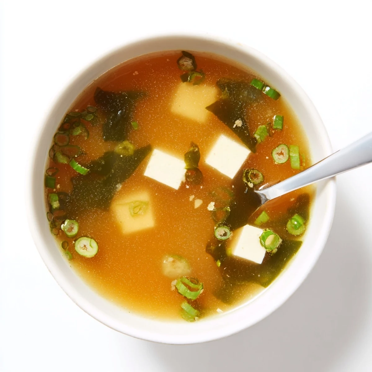 Steaming bowl of easy authentic miso soup with silken tofu cubes and wakame seaweed garnished with fresh green onions