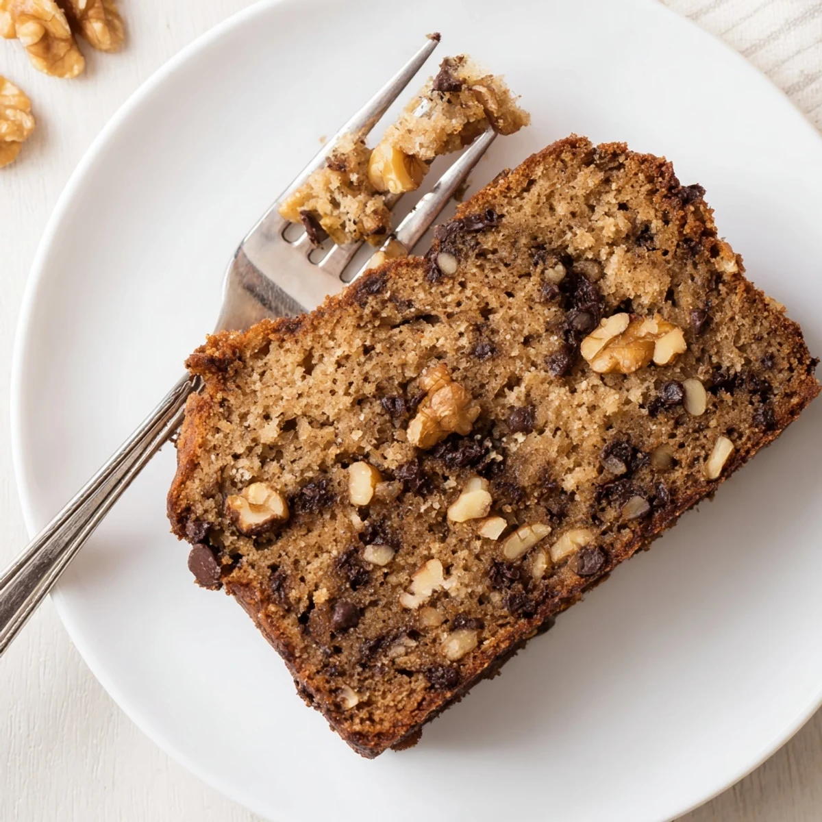 Golden brown keto banana bread loaf sliced on a wooden cutting board with walnuts