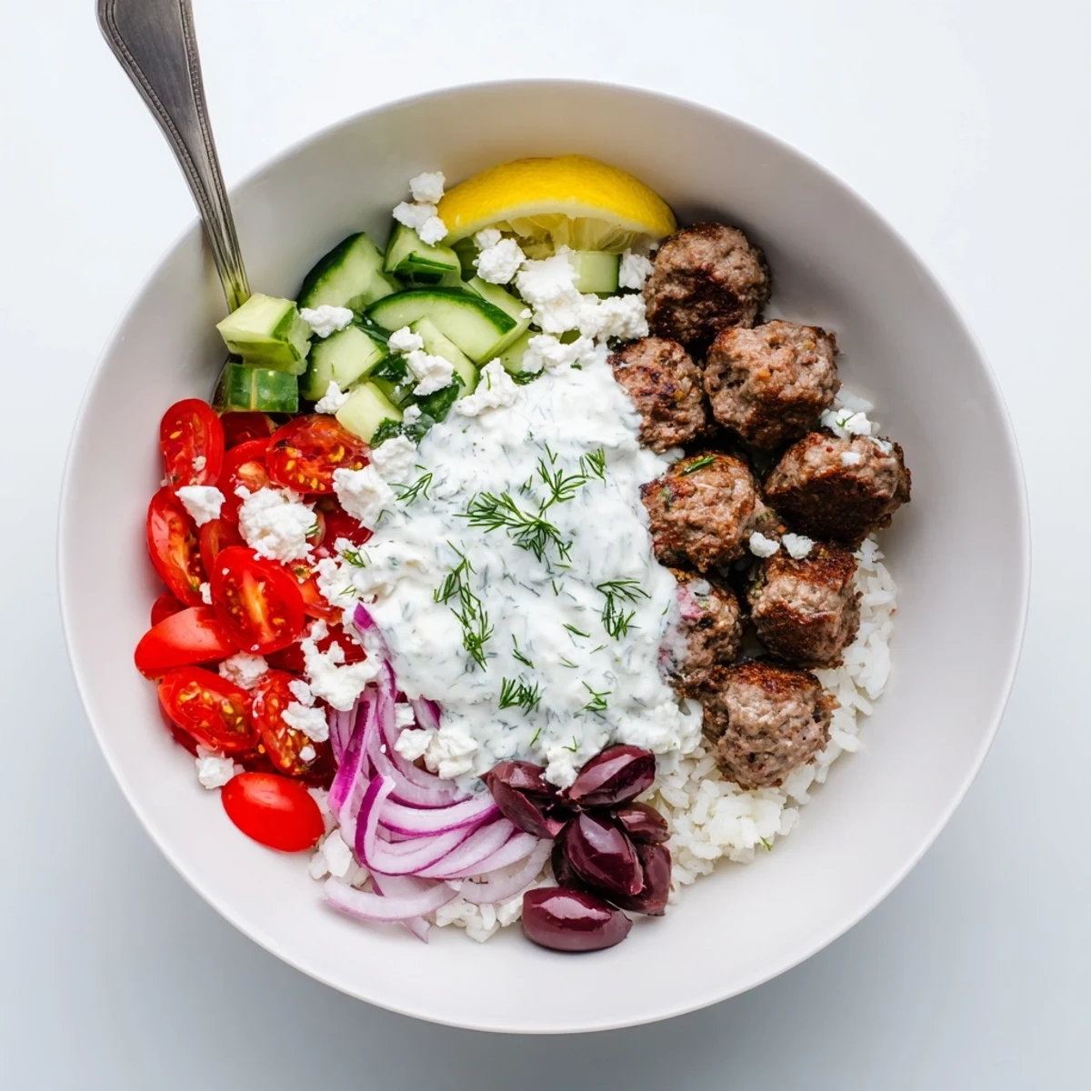 A vibrant Greek meatball bowl topped with tangy tzatziki and fresh lemon wedges