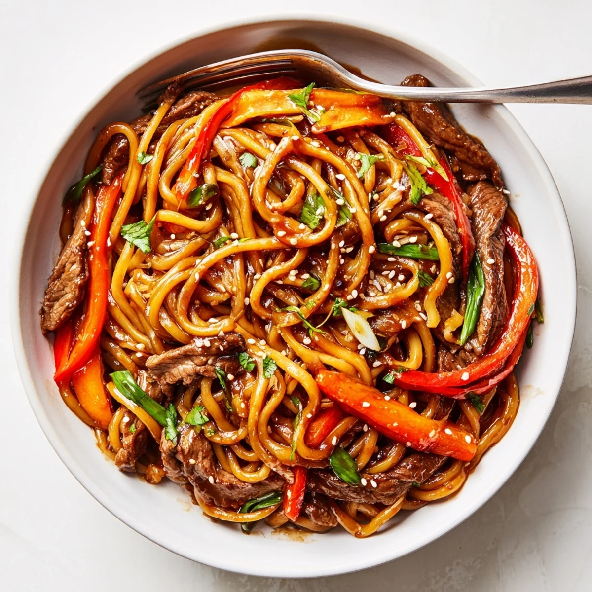 Chopsticks lifting Sticky Beef Noodles, chewy strands coated in sweet-savory sauce