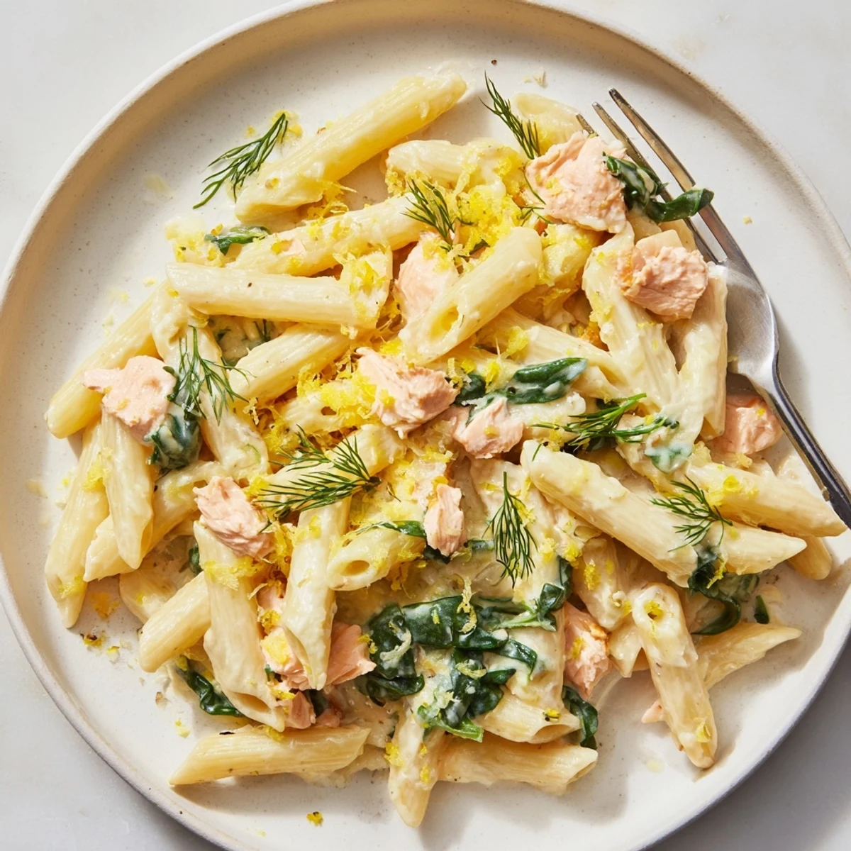 Steaming bowl of creamy salmon penne garnished with fresh dill and lemon zest on a rustic table