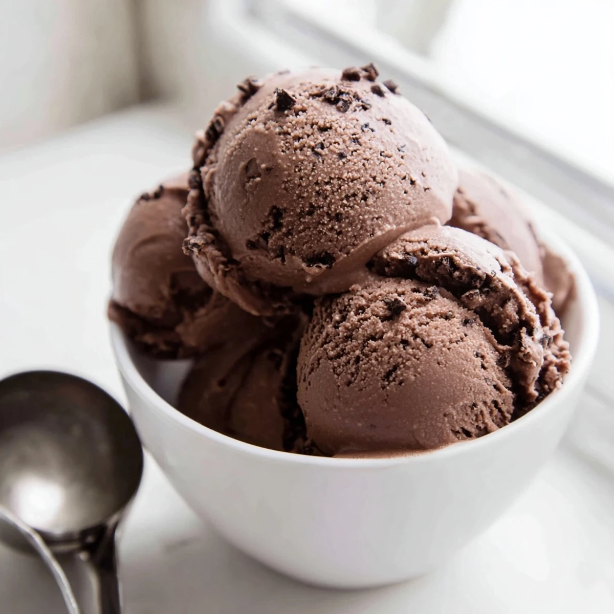 Rich dark chocolate sourdough ice cream swirled in a white ceramic bowl topped with toasted nuts and cocoa dust