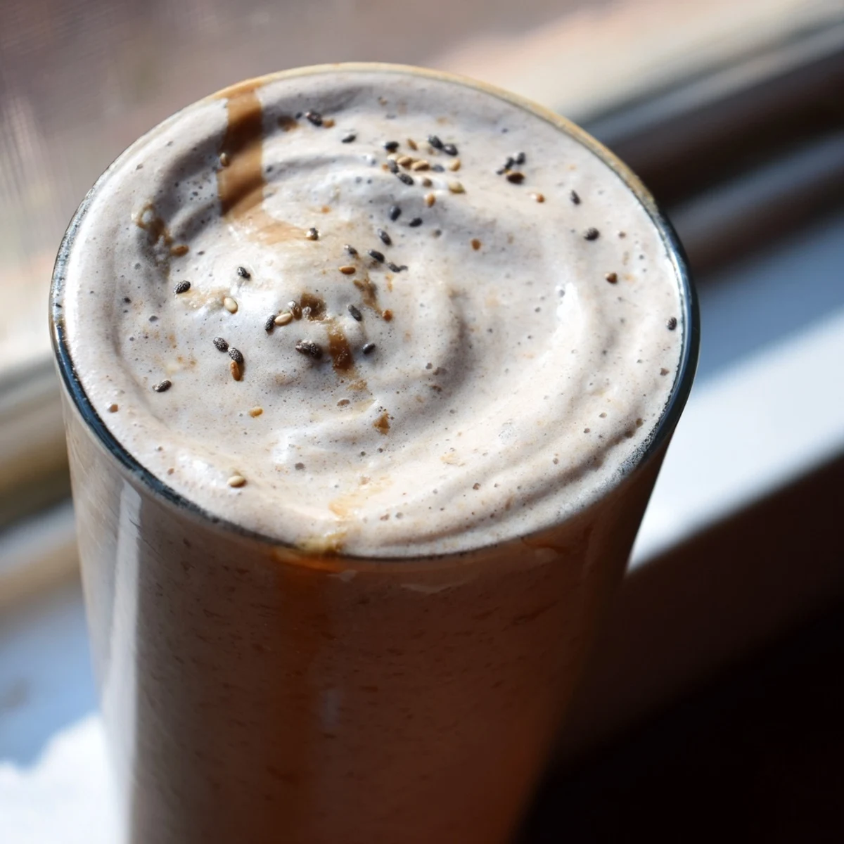 Creamy banana protein coffee smoothie topped with chia seeds in a tall glass