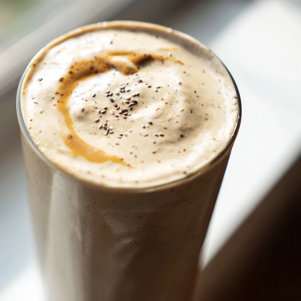 Frothy banana protein coffee smoothie garnished with cinnamon beside a spoon on a napkin
