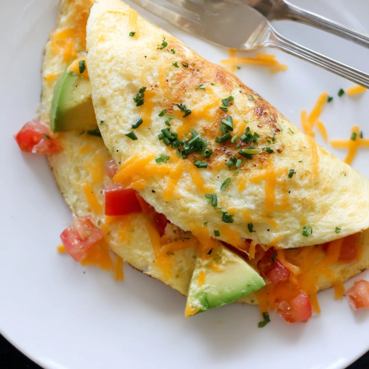 Golden avocado cheesy tomato omelette folded with melted cheddar and fresh vegetables
