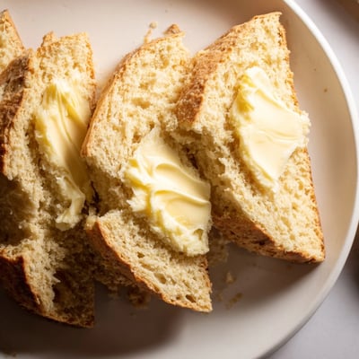 Warm slices of Soda Bread with Irish Butter are shown on a rustic cutting board, with a generous pat of butter melting on top.