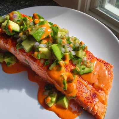 Creamy bang bang salmon with avocado cucumber salsa served over fluffy steamed white rice